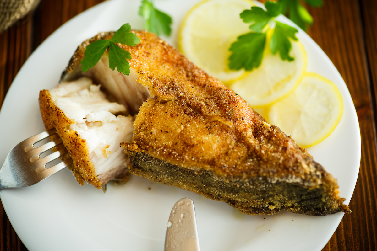 Ikan keli goreng di atas pinggan dengan lemon dan herba