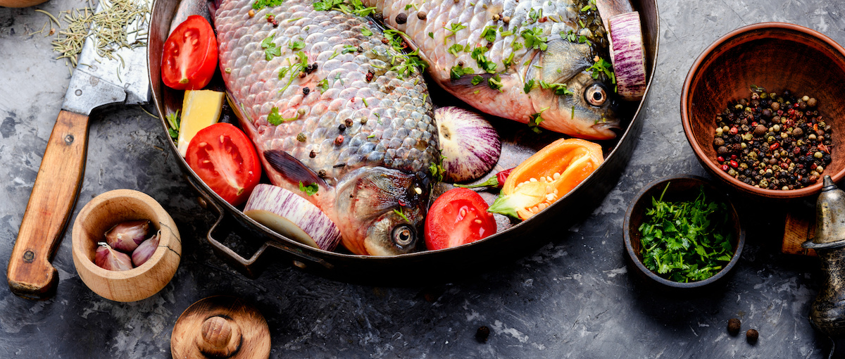 Ikan mas ikan mentah dalam kuali dengan bawang tomato dan sitrus