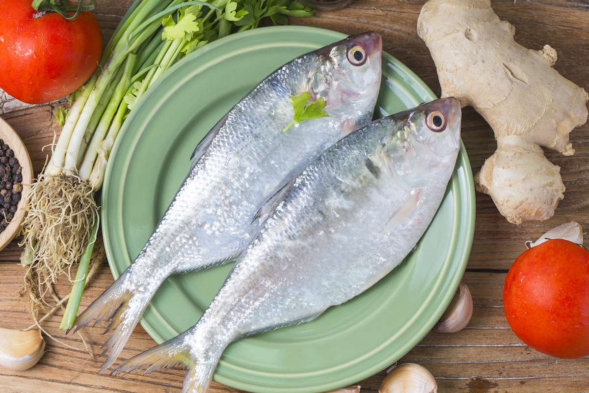 Raw Shad zivis uz zaļas plāksnes ar neapstrādātiem dārzeņiem un sastāvdaļām